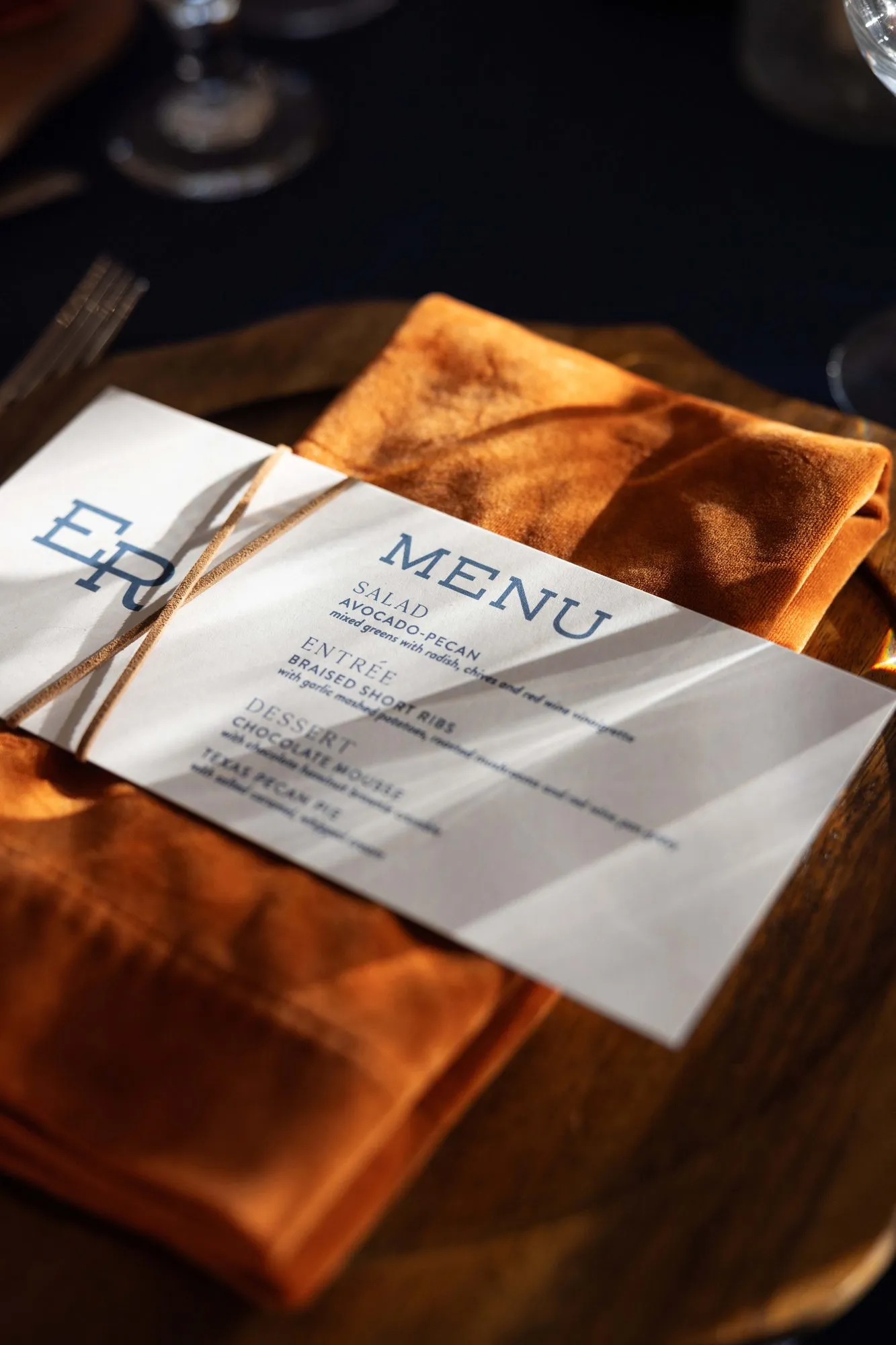 Eliza vellum menu tied with leather cord over a rust velvet napkin in low evening light