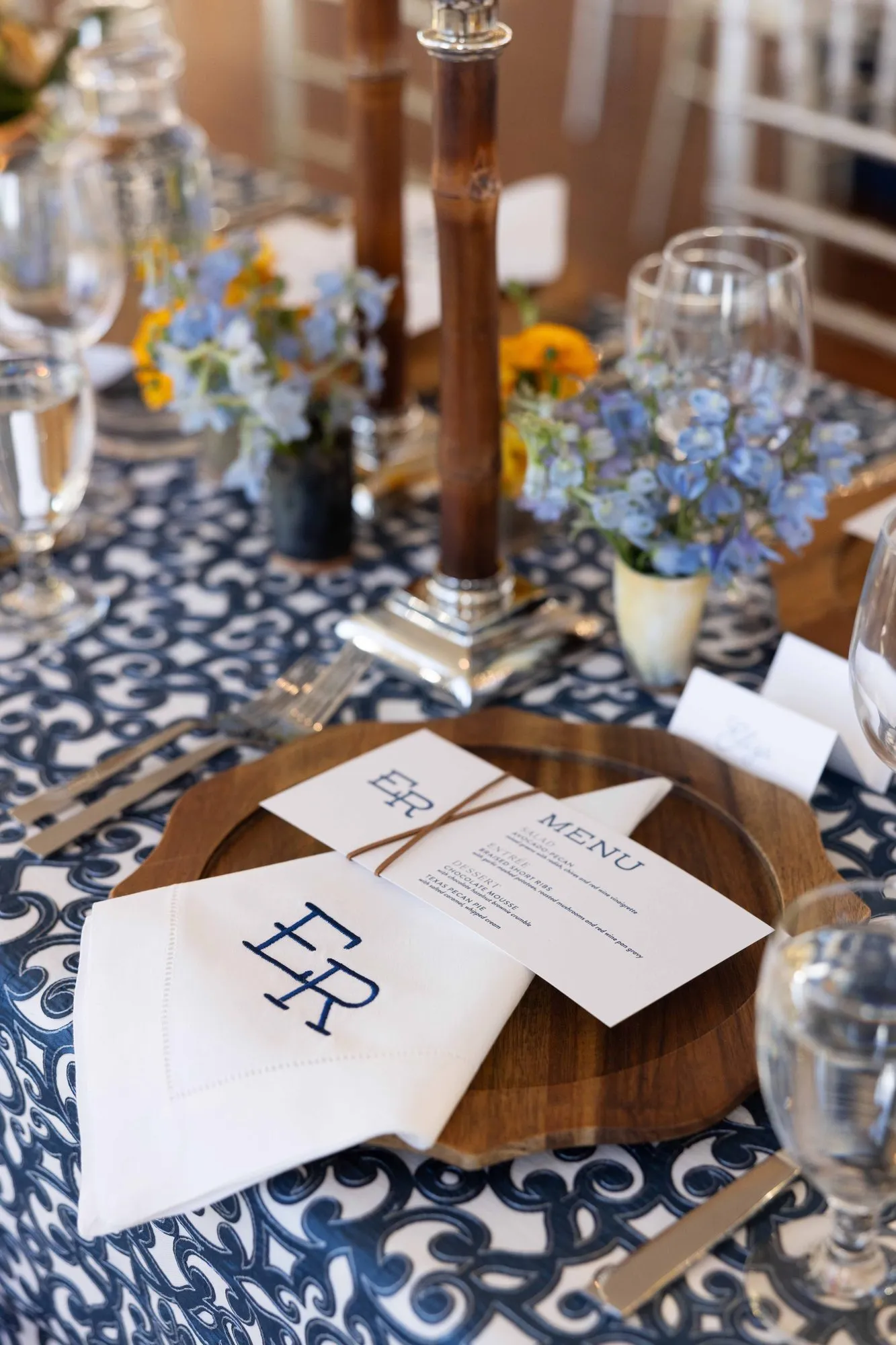 Eliza place setting: monogrammed napkin and vellum menu on a wooden charger over a navy block-print cloth