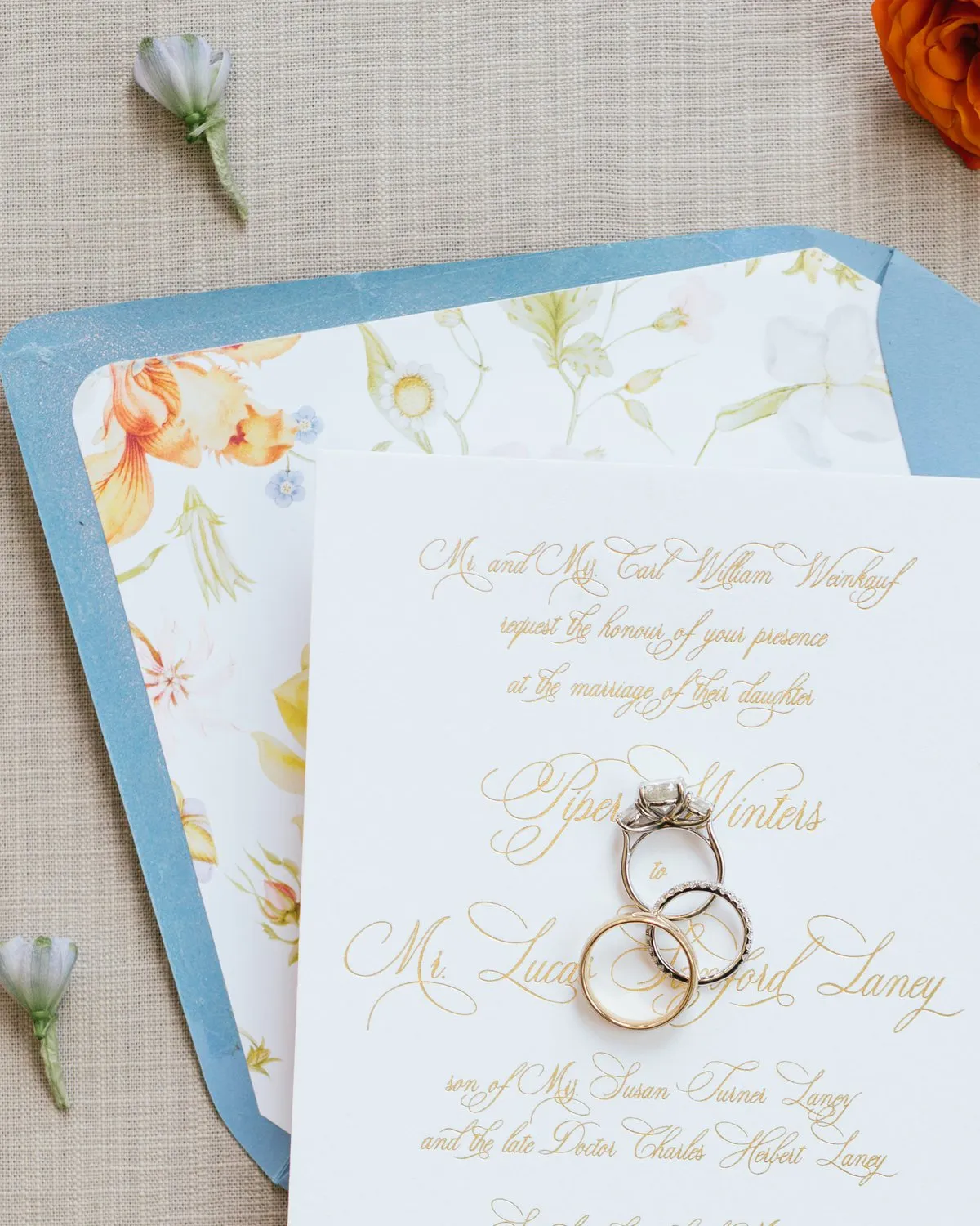 Dusty blue Laney envelope opened to a watercolor garden floral liner, with the gold script invitation resting on top