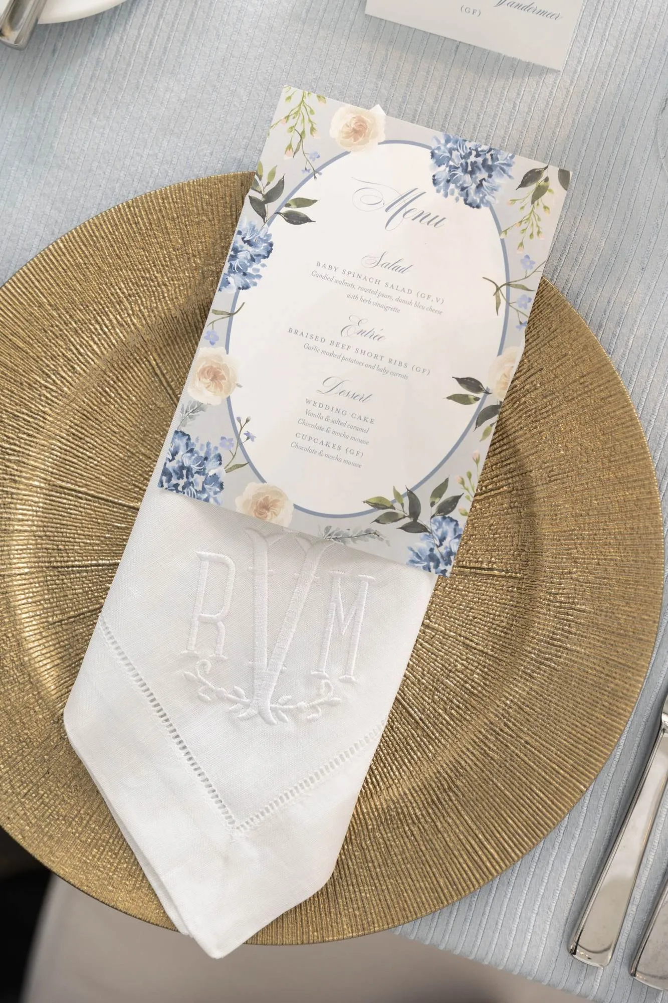 Orr reception place setting with a watercolor floral menu on a gold charger and a monogrammed linen napkin