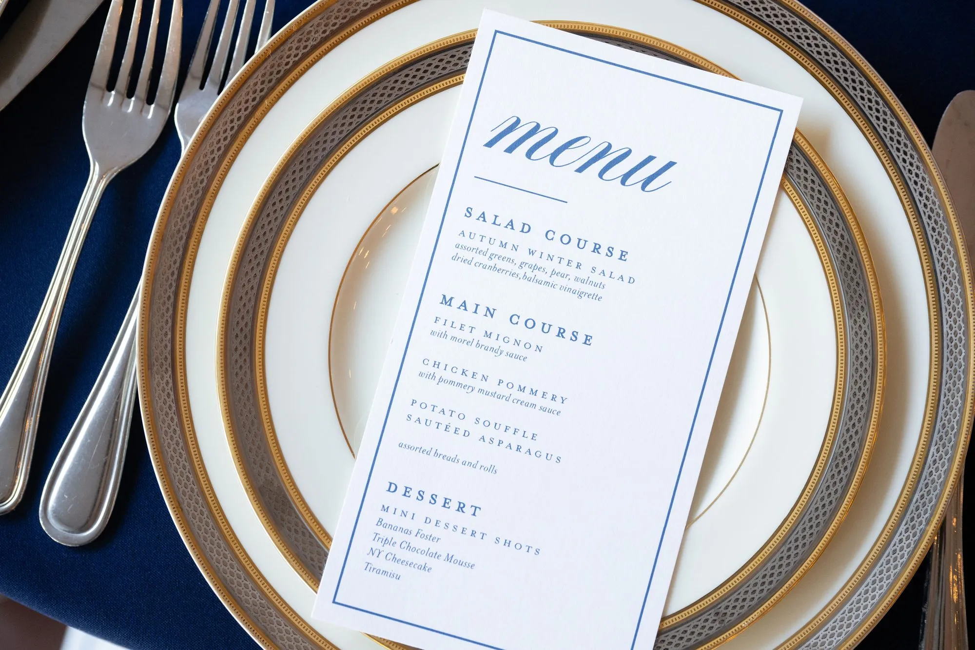 Orr rehearsal dinner menu in royal blue on white, set on gold-rimmed china over navy linen