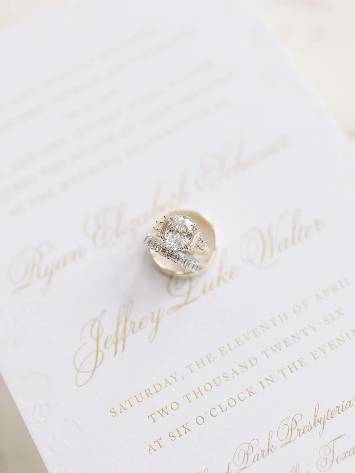 An engagement ring and wedding band resting on the Walter invitation, close in raking light
